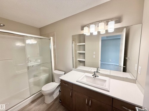 Bathroom featuring a full vanity with an integrated rectangular sink, a shower with sliding glass doors, a toilet, and wood-finish flooring - 22519 96 Avenue, Edmonton, AB 