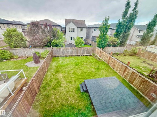Expansive green space featuring a wood fence perimeter, a rectangular hardscaped patio area, mature trees, and landscaping elements - 22519 96 Avenue, Edmonton, AB 