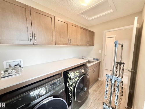 Dedicated laundry room featuring wood-finish cabinetry, a utility sink, and ample countertop space - 22519 96 Avenue, Edmonton, AB 