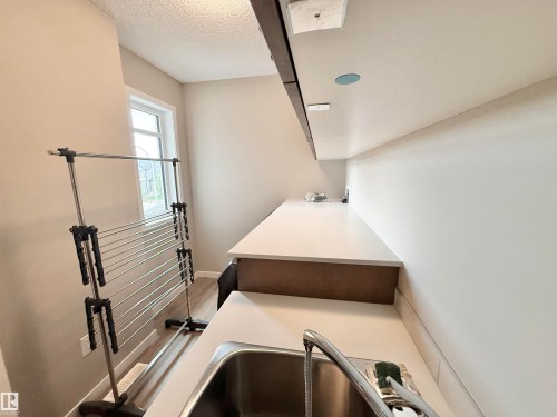 Utility room featuring a stainless steel sink with a chrome faucet, white countertops, built-in lower cabinetry with a wood-finish, and overhead recessed lighting - 22519 96 Avenue, Edmonton, AB 