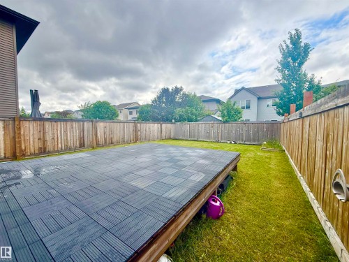 Spacious backyard featuring a large raised deck with dark interlocking tiles, natural wood privacy fencing, and a surrounding lawn area - 22519 96 Avenue, Edmonton, AB 