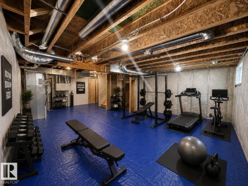 Expansive basement area featuring blue rubber flooring, exposed ceiling joists, white insulated walls, and visible HVAC ductwork - 22519 96 Avenue, Edmonton, AB 