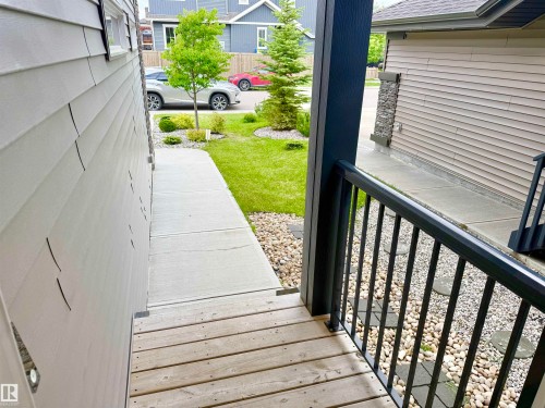 Front entry featuring a wooden deck with black metal railings, a concrete walkway, and gravel landscaping with stepping stones - 22519 96 Avenue, Edmonton, AB 