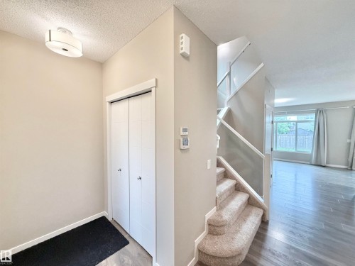 Entryway featuring neutral wall tones, a modern flush-mount ceiling light, white bi-fold closet doors, and carpeted stairs with a white and glass railing - 22519 96 Avenue, Edmonton, AB 