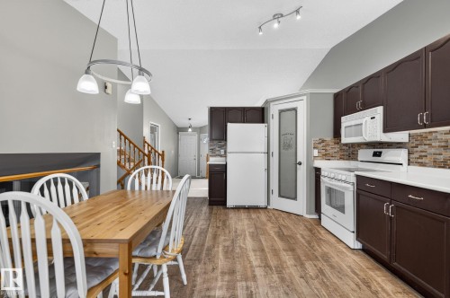 Kitchen and dining area featuring wood-finish flooring, vaulted ceilings, dark cabinetry, light countertops, and a mosaic tile backsplash - 6225 159A Avenue, Edmonton, AB 