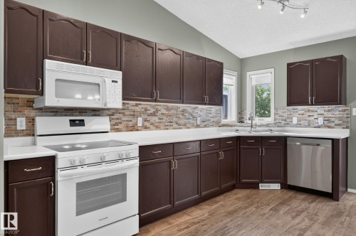 Kitchen featuring dark wood-finish cabinetry, white countertops, and a mosaic tile backsplash - 6225 159A Avenue, Edmonton, AB 