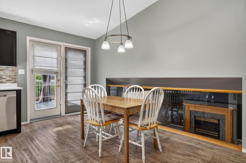 Dining area featuring wood-finish flooring, a contemporary chandelier, and a built-in fireplace with a stone surround - 6225 159A Avenue, Edmonton, AB 