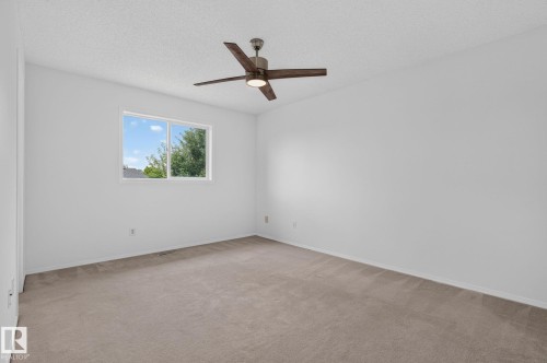 Spacious room featuring neutral carpeting, white painted walls, a large window with white trim, and a ceiling fan with light fixture - 6225 159A Avenue, Edmonton, AB 