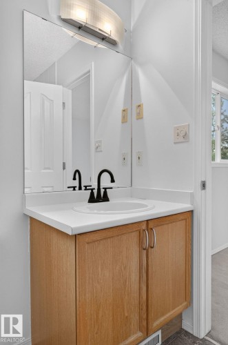 Bathroom vanity featuring light wood-finish cabinetry, a white countertop, an undermount sink, and a matte black faucet - 6225 159A Avenue, Edmonton, AB 