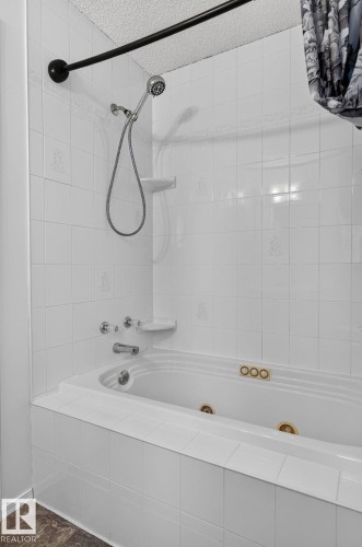 White tiled bathtub with an integrated whirlpool system featuring gold-toned jets and controls - 6225 159A Avenue, Edmonton, AB 