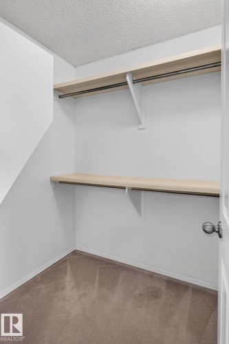 Walk-in closet featuring two levels of wood-finish shelving and metal hanging rods - 6225 159A Avenue, Edmonton, AB 