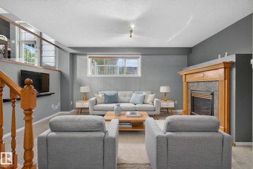 Living space featuring a wood-mantled fireplace with a stone surround, a window with blinds, and a built-in television shelf - 6225 159A Avenue, Edmonton, AB 