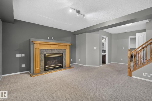 Carpeted room featuring a fireplace with a light wood mantel and stone surround - 6225 159A Avenue, Edmonton, AB 