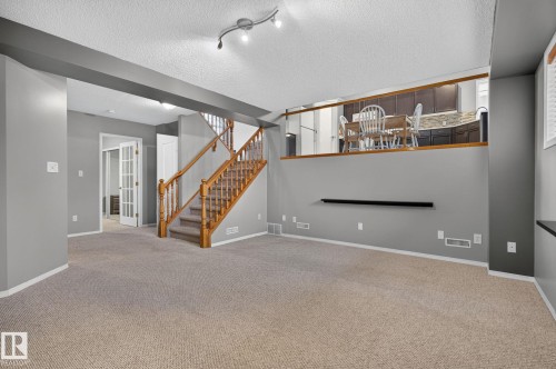 Lower level featuring light-toned carpeting, a light wood staircase with balusters, and a half-wall offering a glimpse of the kitchen - 6225 159A Avenue, Edmonton, AB 