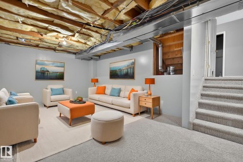 Lower-level living area featuring light gray wall paint, exposed ceiling insulation, wood ceiling beams, and a carpeted staircase - 6225 159A Avenue, Edmonton, AB 