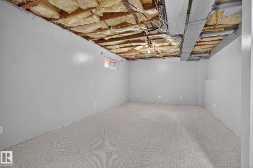 Spacious room featuring light gray walls, textured carpet flooring, and exposed ceiling joists with insulation - 6225 159A Avenue, Edmonton, AB 