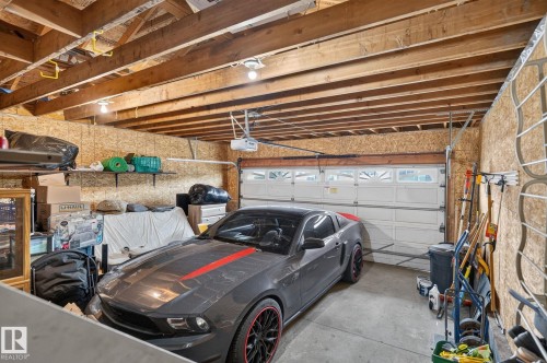 Spacious garage with exposed wood beam ceiling, paneled walls, and a white overhead door with upper window inserts - 6225 159A Avenue, Edmonton, AB 