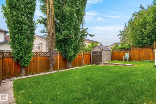 Expansive backyard featuring a lush lawn, perimeter wood fencing with lattice top, mature trees, a durable storage shed, and a raised garden bed with stone retaining wall - 6225 159A Avenue, Edmonton, AB 