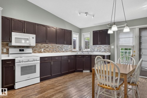 Open-concept kitchen and dining area featuring rich dark wood-finish cabinetry, white countertops, and a mosaic tile backsplash - 6225 159A Avenue, Edmonton, AB 