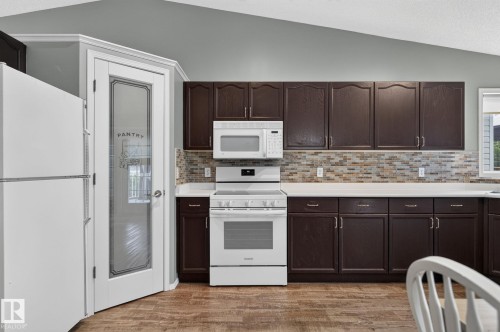 Kitchen featuring dark wood cabinetry, white countertops, a mosaic tile backsplash, wood-finish flooring, and a glass-paneled pantry door - 6225 159A Avenue, Edmonton, AB 