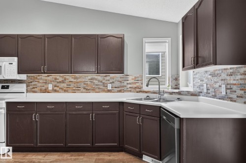 Kitchen featuring dark wood-finish cabinetry, white countertops, and a mosaic tile backsplash - 6225 159A Avenue, Edmonton, AB 