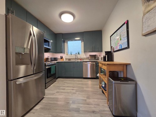 Galley kitchen featuring full-height teal cabinetry, stainless steel appliances, light-toned countertops, and wood-finish flooring - 2514 149 Avenue, Edmonton, AB 