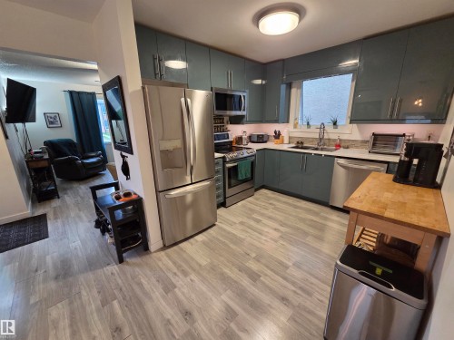 Kitchen featuring sleek blue-gray cabinetry, stainless steel appliances, and wood-finish flooring - 2514 149 Avenue, Edmonton, AB 