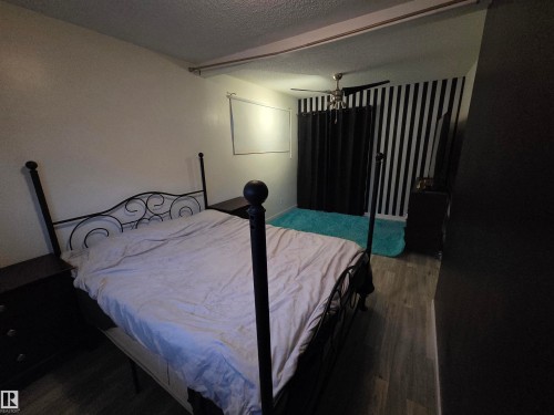 Room featuring wood-finish flooring, a ceiling fan with integrated lighting, and a prominent accent wall with vertical stripes - 2514 149 Avenue, Edmonton, AB 