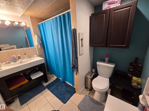 Bathroom featuring a dark wood-finish vanity with an integrated basin, a ceramic tile shower surround, a white toilet, and dark wood-finish wall-mounted cabinetry - 2514 149 Avenue, Edmonton, AB 