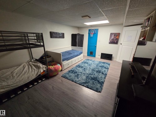 Spacious room featuring wood-finish flooring, a suspended ceiling, and a bright blue door - 2514 149 Avenue, Edmonton, AB 