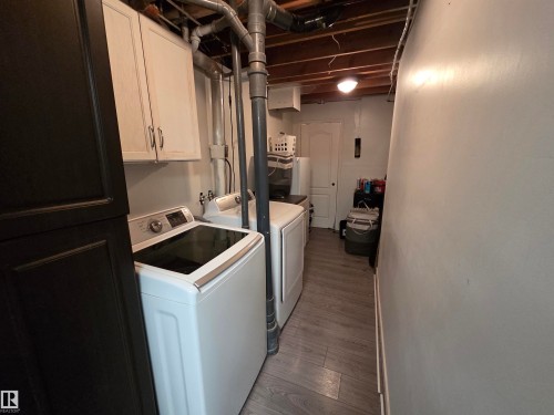 Laundry area featuring a washer and dryer, wood-finish flooring, white wall cabinets, and exposed ceiling joists - 2514 149 Avenue, Edmonton, AB 