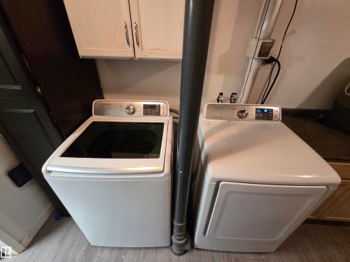 Laundry area featuring wood-finish flooring, white cabinetry with silver-tone hardware, and a dark countertop - 2514 149 Avenue, Edmonton, AB 