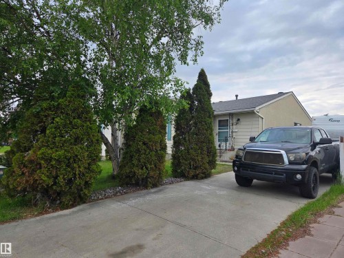 Front exterior featuring a concrete driveway, mature evergreen trees, and a birch tree - 2514 149 Avenue, Edmonton, AB 