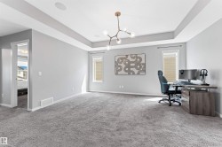Carpeted room featuring a tray ceiling with a modern chandelier, recessed lighting, and two tall windows with blinds - 