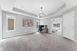 Spacious room featuring tray ceilings, recessed lighting, and a contemporary chandelier - 