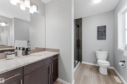 Bathroom featuring a dual-sink vanity with a light-toned countertop, dark wood-finish cabinetry, a glass-enclosed shower with dark tile surround, a toilet, and wood-finish flooring - 
