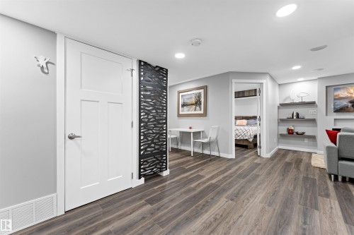 Spacious room featuring wood-finish flooring, recessed lighting, and a contemporary decorative screen - 9664 223 Street, Edmonton, AB 