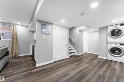 Finished lower level featuring wood-finish flooring, recessed lighting, and a built-in laundry center with stacked appliances - 