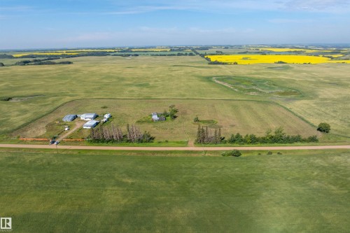 Expansive agricultural land featuring multiple outbuildings, a gravel road, and surrounding cultivated fields, with distant yellow crops - 534072 Range Road 85, Rural Two Hills County, AB 