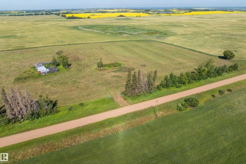 Expansive agricultural land featuring a gravel road, mature trees, and multiple outbuildings - 534072 Range Road 85, Rural Two Hills County, AB 