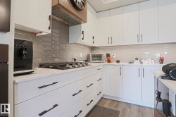 Modern kitchen featuring white cabinetry, a gas cooktop, quartz countertops, and a gray geometric tile backsplash - 