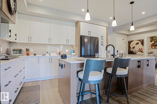 Modern kitchen featuring a central island with seating, pendant lighting, and a matte black faucet - 211 7463 May Common, Edmonton, AB 