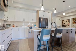 Modern kitchen featuring a central island with seating, pendant lighting, and a matte black faucet - 