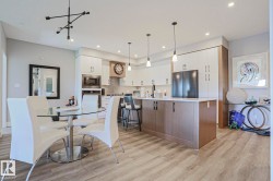 Open-concept kitchen and dining area featuring wood-finish flooring, two-tone cabinetry, a large kitchen island with pendant lighting, and stainless steel appliances - 