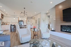 Open-concept living space featuring wood-finish flooring, a contemporary kitchen with white cabinetry, a built-in fireplace, recessed lighting, and modern pendant light fixtures - 