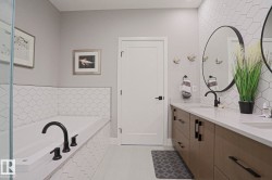 Contemporary bathroom featuring a large soaking tub with black fixtures, a dual vanity with wood-finish cabinetry, white countertops, and circular mirrors - 