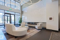 Lobby featuring a grand fireplace with a large-format tile surround, contemporary circular pendant lighting, full-height windows, a glass entry door, and large dark floor tiles - 