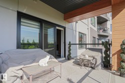 Spacious outdoor balcony featuring a patterned area rug, black metal and glass railing, and a wood-finish ceiling accent - 