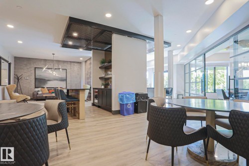 Spacious communal area featuring light wood-finish flooring, recessed lighting, and a prominent glass wall - 211 7463 May Common, Edmonton, AB 