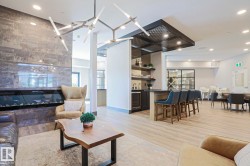 Open-concept common area featuring a linear fireplace with a stone-look surround, a built-in bar with bar seating, wood-finish flooring, and contemporary lighting fixtures - 